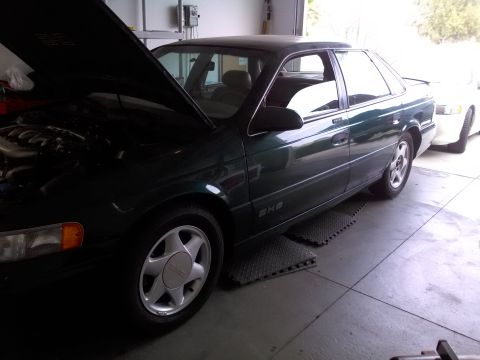 1993 Ford Taurus - A dark green 1993 Ford Taurus sedan is parked in a garage with its hood up, next to a white vehicle.