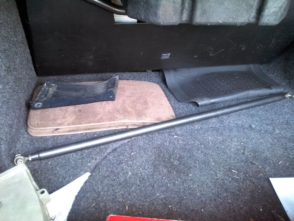 Interior trunk with metal bar, floor mats, and a black plastic piece
