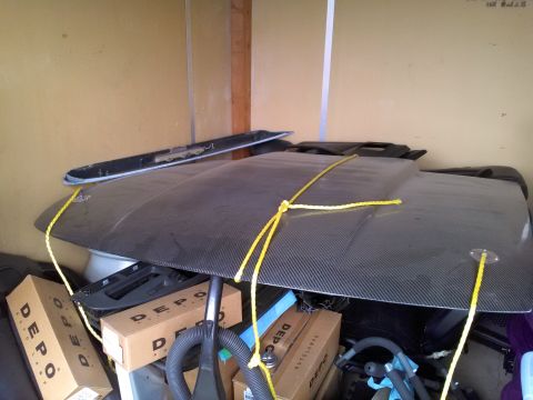 1993 Ford Taurus - A carbon fiber hood is stored with boxes and other car parts in a cluttered space.