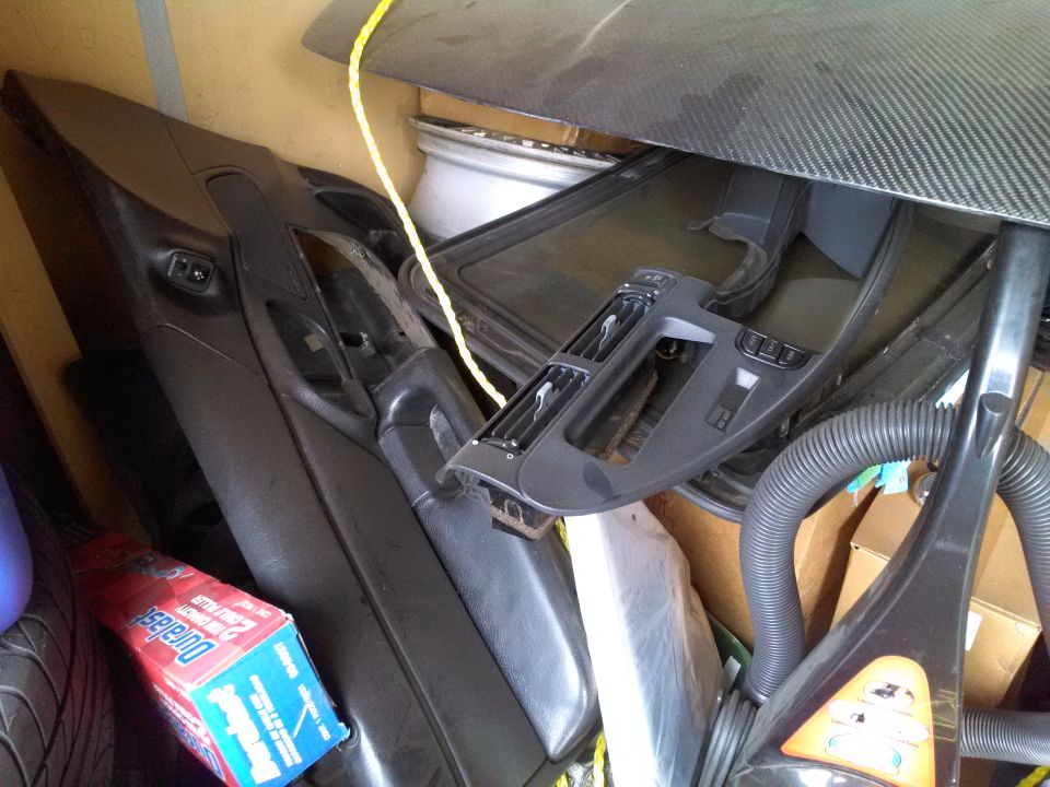 Car door panel and dashboard trim pieces piled with a vacuum cleaner and a box of Duralast brake pads