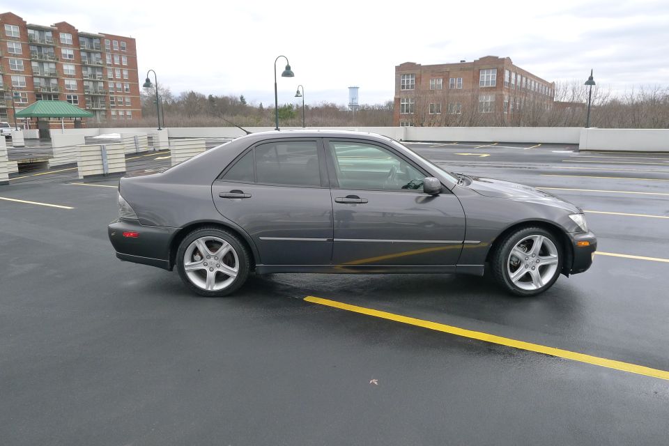 Dark gray 2002 Lexus IS 300 sedan parked on a wet asphalt surface, viewed from the side