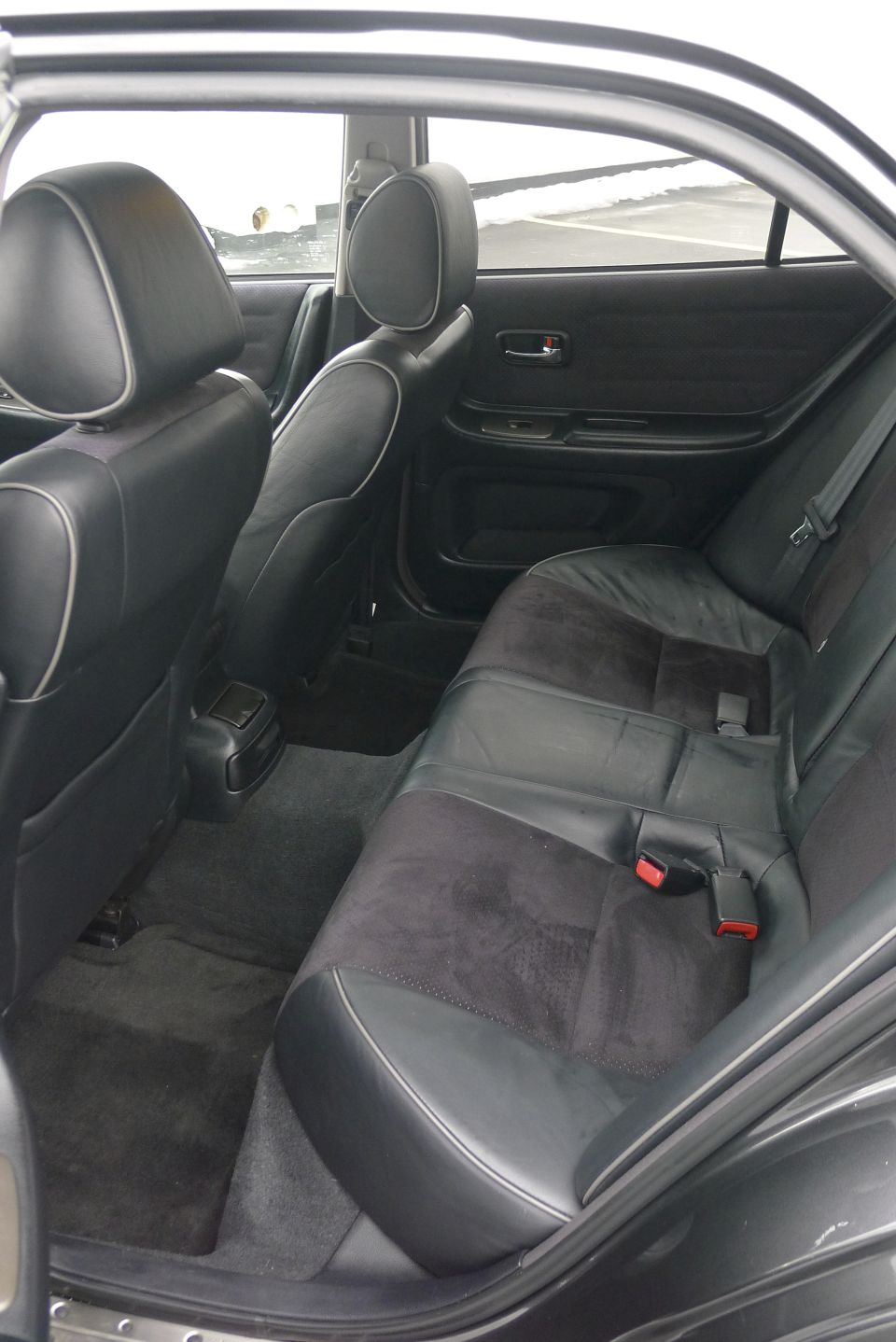 Back seat of a 2002 Lexus IS 300, showing black leather and suede seats with red seatbelt buckles