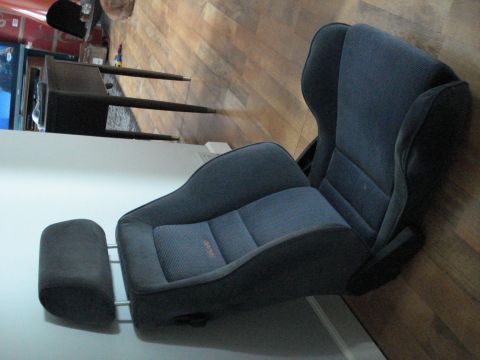 1972 Ford Pinto - A dark gray car seat with an adjustable headrest is shown indoors, with orange stitching on the seat cushion.