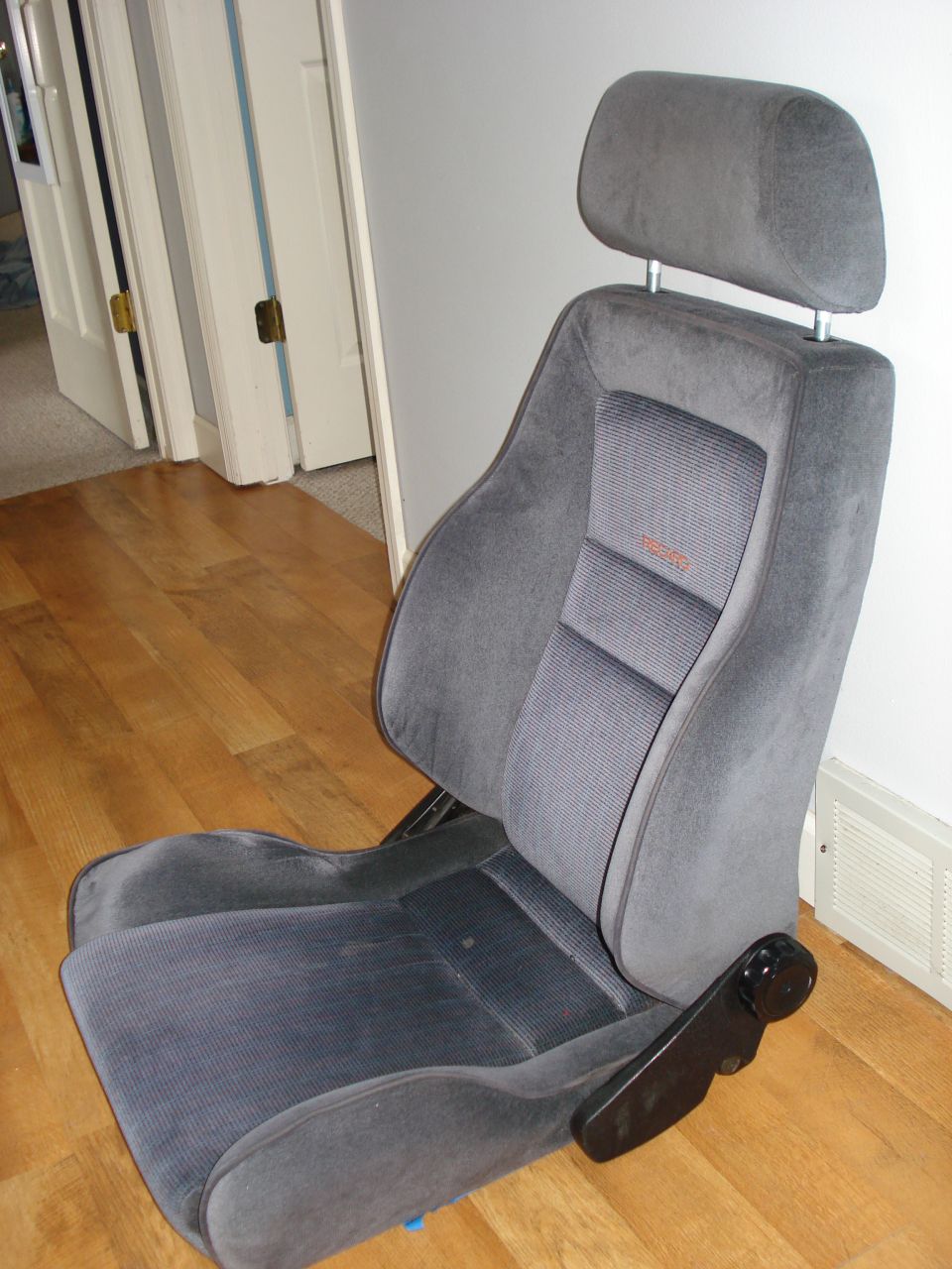 Gray fabric car seat with headrest and orange 'RECARO' logo on the backrest