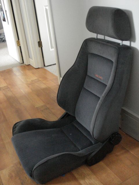 1972 Ford Pinto - A gray Recaro car seat with an orange logo is shown from the side against a wall.