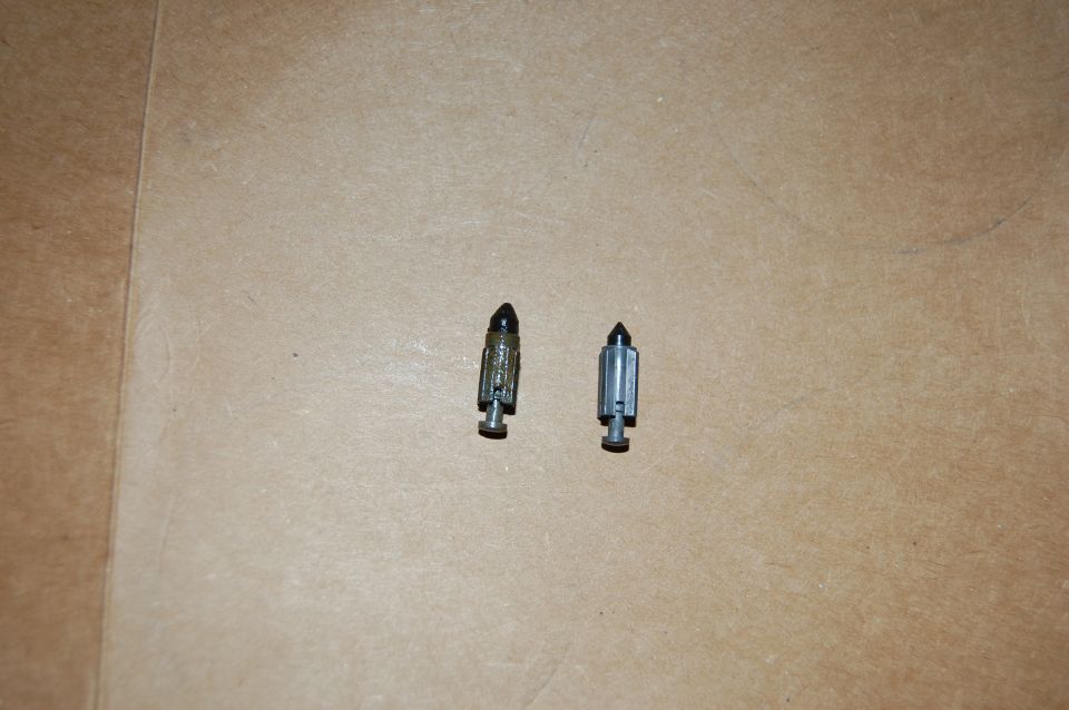 Two carburetor float needles on a tan surface