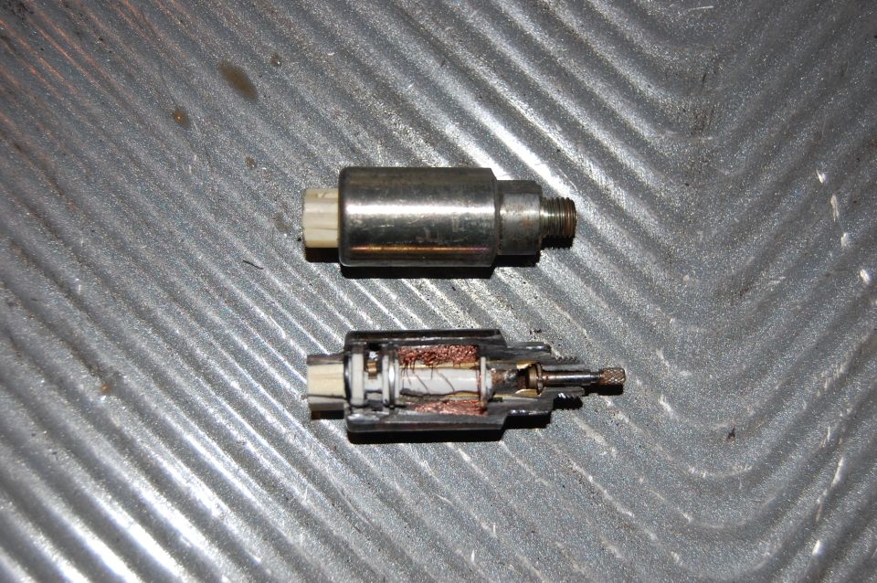 Two metal electrical components, one cut open showing copper wiring, on a textured surface