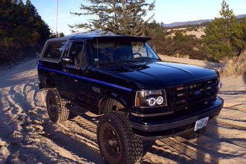 1992 Ford Bronco - This black 1992 Ford Bronco, a distinctive blue stripe, navigates sandy dunes.