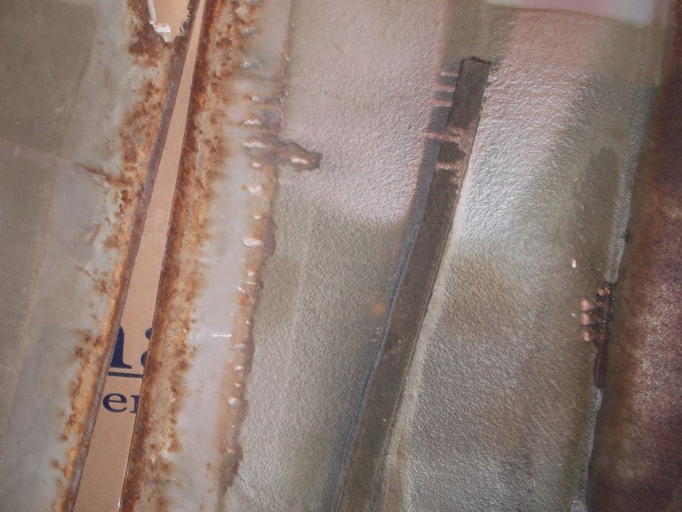 Close-up of a rusty interior car panel with some text visible on a piece of cardboard
