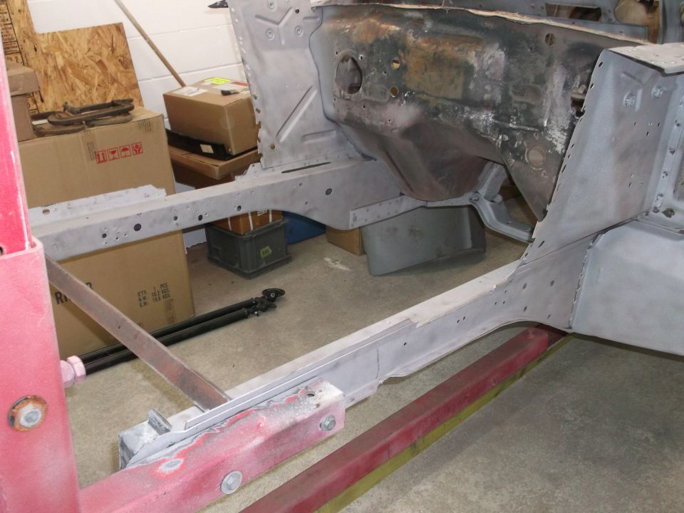 Bare-metal Mustang body shell on a red rotisserie jig during restoration in a garage