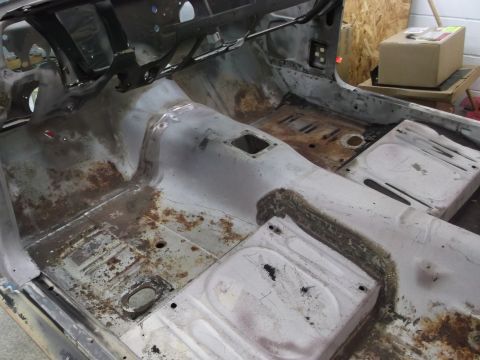 1967 Ford Mustang - The interior of a car is shown stripped down, revealing extensive rust on the floor pans and seat mounts.