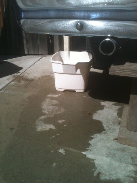 1964 Ford Ranchero - A white bucket is placed under a vehicle's exhaust pipe to catch dripping fluid.