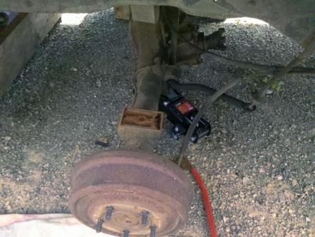 1982 Ford Bronco - Rear axle and brake drum assembly with a jack supporting the vehicle.