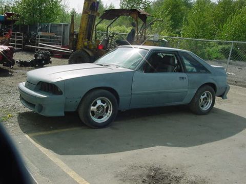 1990 Ford F-150 - A gray Ford Mustang coupe sits in an outdoor lot, awaiting restoration, with a forklift visible behind it.