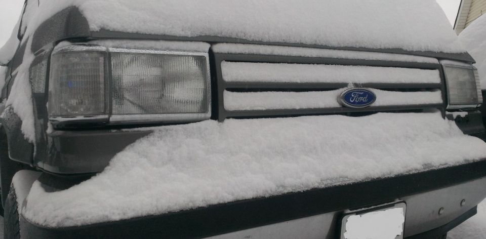 1987 Ford Bronco front end covered in snow, showing grille and headlight
