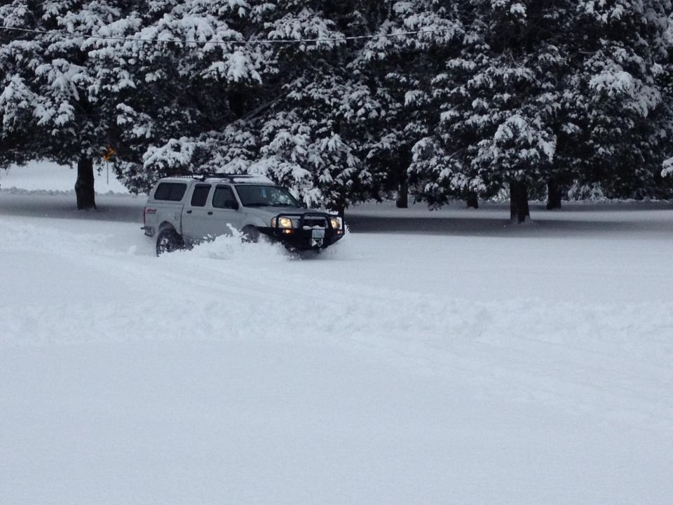 Silver pickup truck with a cap and bull bar driving through deep snow
