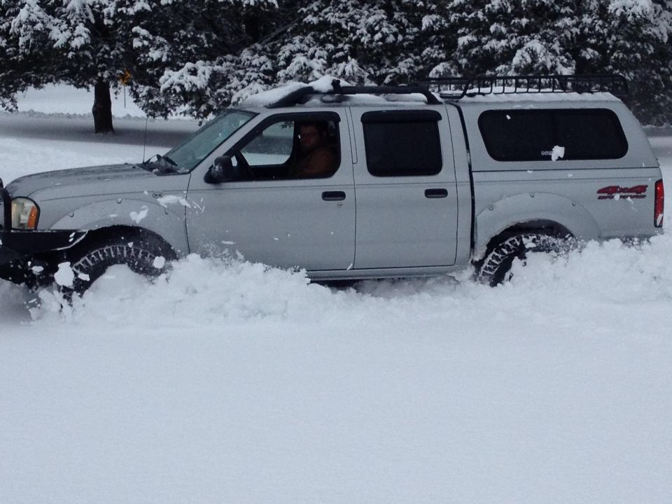 Silver pickup truck with a cap driving through deep snow