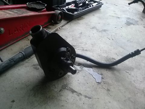 1996 Ford Bronco - A black power steering pump with its associated hose lies on a concrete surface next to a red car jack and a toolbox.