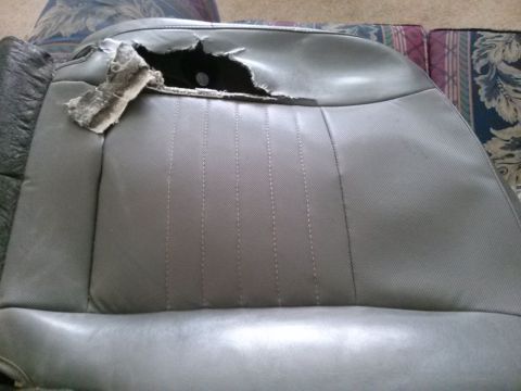 1996 Ford Bronco - The interior of a vehicle shows a gray seat with significant damage to the upholstery, revealing underlying materials.