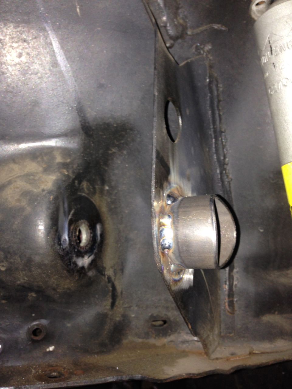Close-up of a metal bracket welded onto a car's frame, showing weld marks and a circular opening