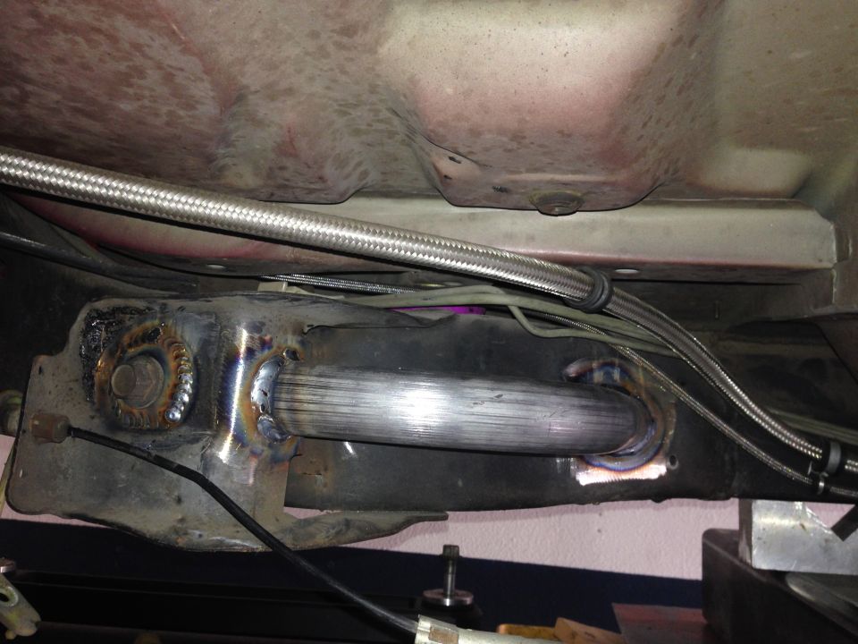 Underside of a vehicle showing a custom exhaust pipe welded to the frame, with braided metal lines above