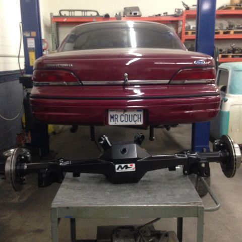 1992 Ford Crown Victoria - Rear view of a maroon Ford Crown Victoria LX on a lift, undergoing maintenance with its rear axle detached.