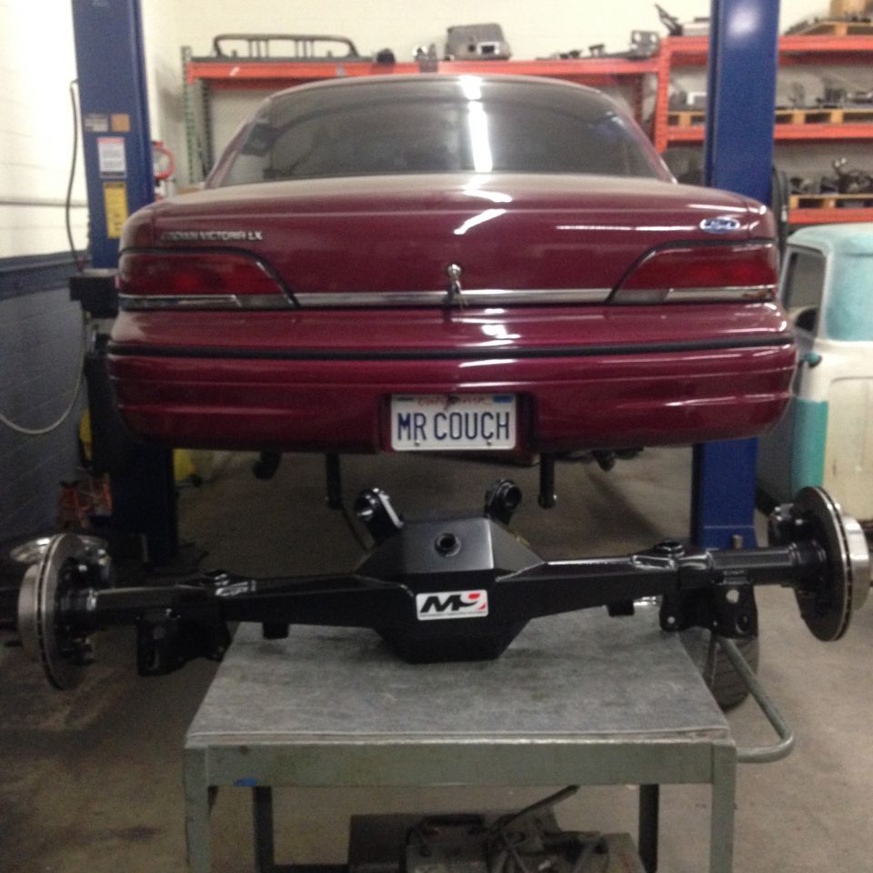 Maroon Ford Crown Victoria LX with "MR COUCH" license plate, raised on a lift with rear axle removed