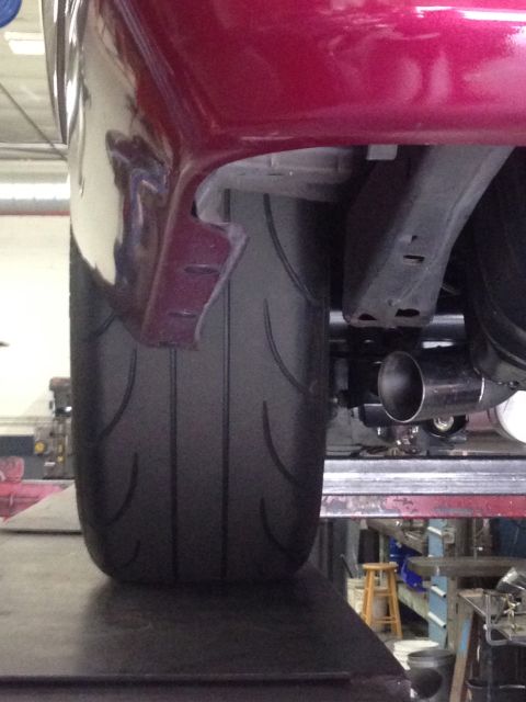 1992 Ford Crown Victoria - Close-up view of a wide rear tire and exhaust pipe on a red vehicle, possibly undergoing modification.