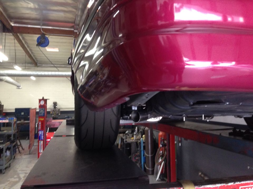 Close-up of a car's rear bumper and tire on a lift. The car is dark red