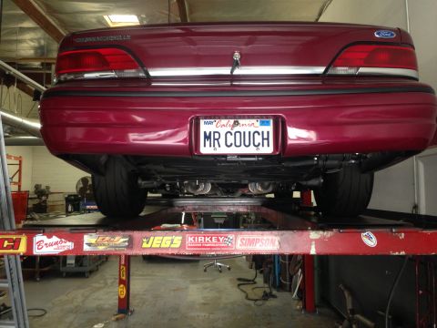 1992 Ford Crown Victoria - Rear view of a red 1992 Ford Crown Victoria on a car lift, displaying a custom exhaust system and a personalized California license plate.
