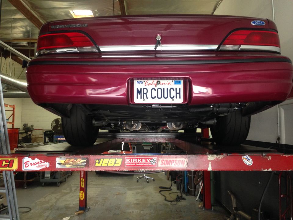 Red 1992 Ford Crown Victoria rear view on a car lift, showing custom exhaust and California license plate 'MR COUCH'