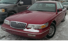 2000 Mercury Grand Marquis - A red Mercury Grand Marquis is parked in a snowy lot, with another vehicle partially visible to its left.