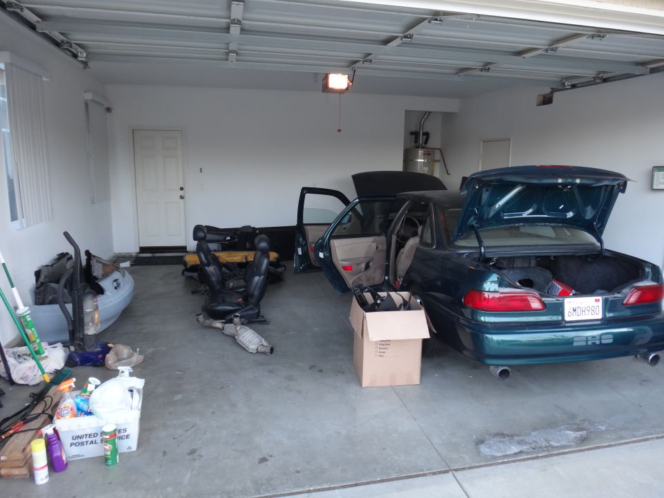 Green sedan with open trunk and doors, interior parts on floor. License plate 6MDH980