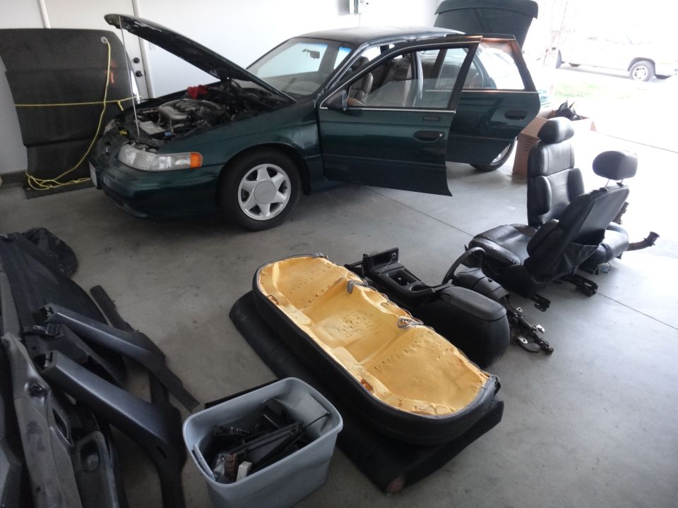 Green station wagon with hood and doors open, interior parts like seats and console are on the floor