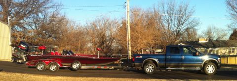 1982 Ford Bronco - A blue pickup truck tows a red boat on a trailer on a sunny day.