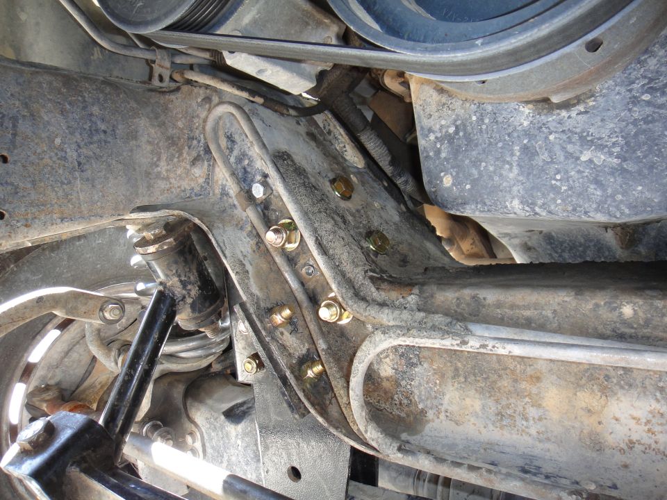 Undercarriage view of front suspension bracket with new gold bolts, sway bar, and steering components on a Bronco.