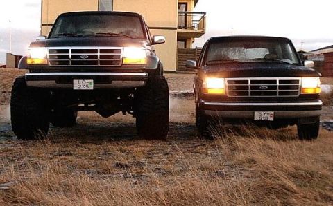 1996 Ford Bronco - Two Ford Broncos are parked side-by-side in a grassy area with a building in the background.