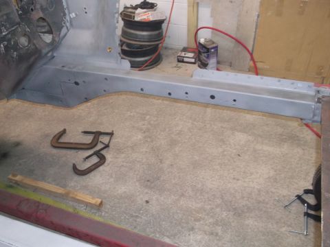 1967 Ford Mustang - The interior of a car chassis is shown with primer applied, along with tools and stacked tires in the background.