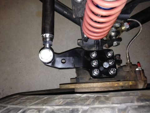 1987 Suzuki Samurai - Close-up of a black steering bracket assembly, a red coil spring and visible bolts.
