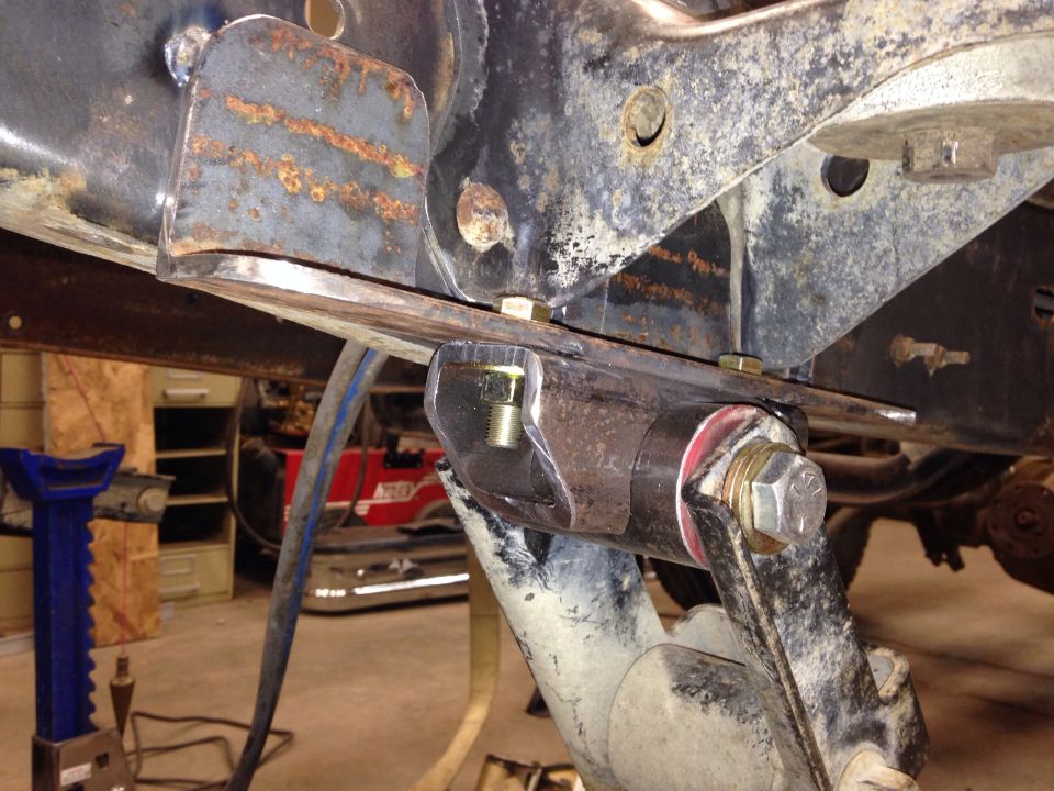Close-up of rusty vehicle frame with suspension parts and bolts, jack stands visible