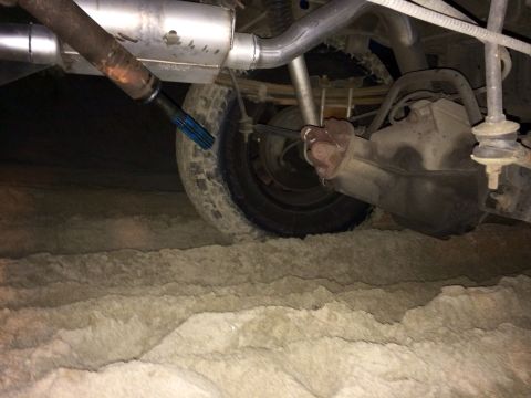 1992 Ford Bronco - Undercarriage view of a vehicle's rear axle and exhaust system, partially obscured by sand.