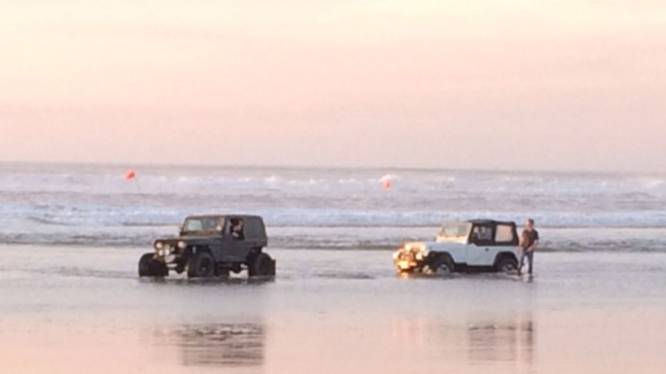 Two Jeep Wranglers driving on a beach at sunset