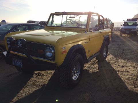 1992 Ford Bronco - First-gen Ford Bronco with aftermarket modifications on a beach, other vehicles nearby.