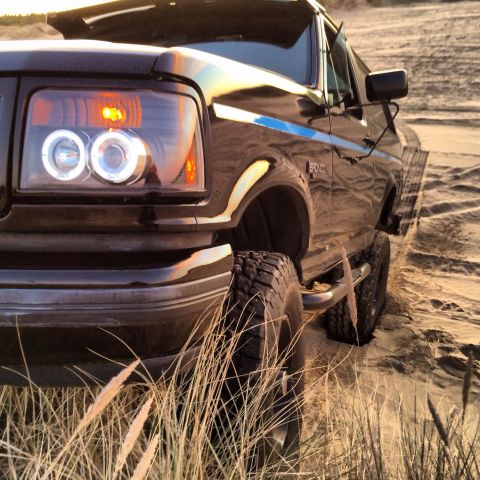 1992 Ford Bronco - A black Ford Bronco is shown from a low angle, with its front quarter visible on a sandy dune.