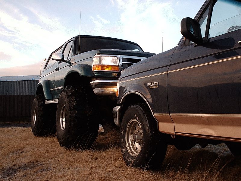 Two lifted Ford Broncos on big off-road tires parked on grass at dusk
