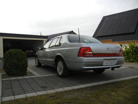 1999 Ford Fairlane - A silver sedan is parked in a driveway next to a garage and a house with solar panels.