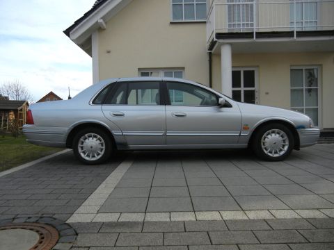 1999 Ford Fairlane - A silver sedan is parked on a paved driveway in front of a house.