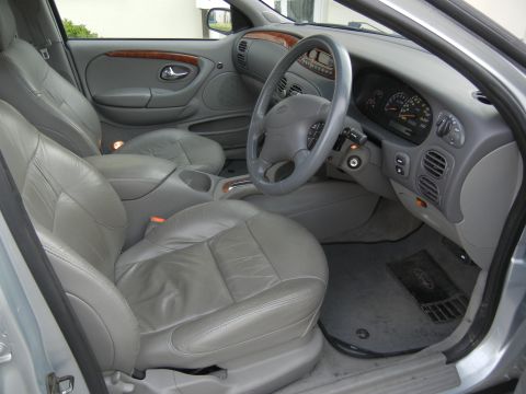 1999 Ford Fairlane - The interior of a silver sedan features leather seats, a wood-trimmed dashboard, and a clear view of the instrument cluster.