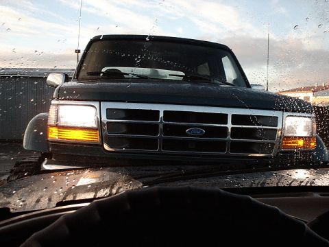 1996 Ford Bronco - Front view of a dark green 1996 Ford Bronco, seen through a wet windshield.
