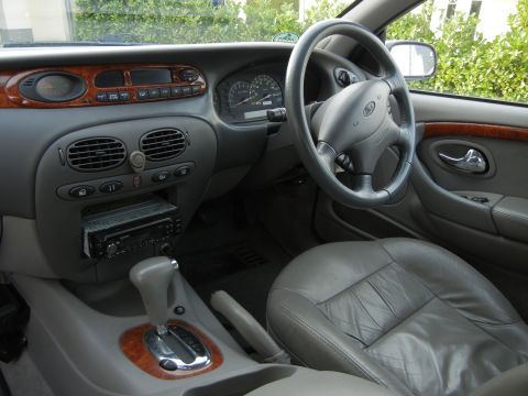 1999 Ford Fairlane - The interior of a car shows the dashboard, steering wheel, gear shifter, and front seats.